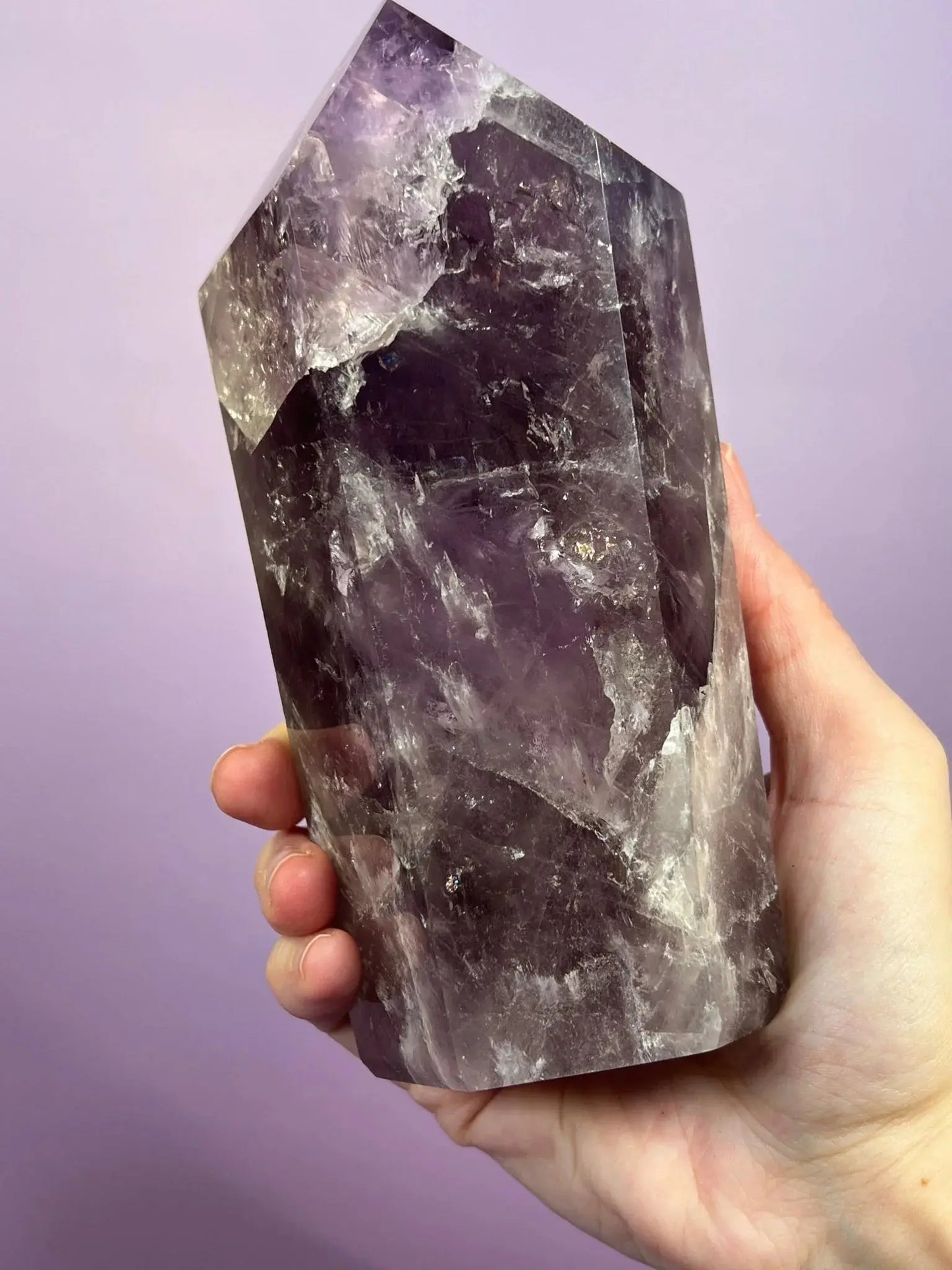 Hand holding a smoky amethyst crystal tower with rainbow flash against a purple background