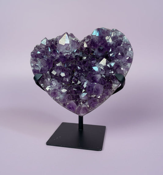 Heart-shaped amethyst crystal on a stand against a light purple background