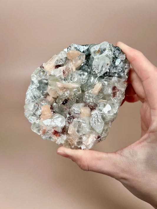 Hand holding apophyllite with peach stilbite and chalcedony mineral cluster