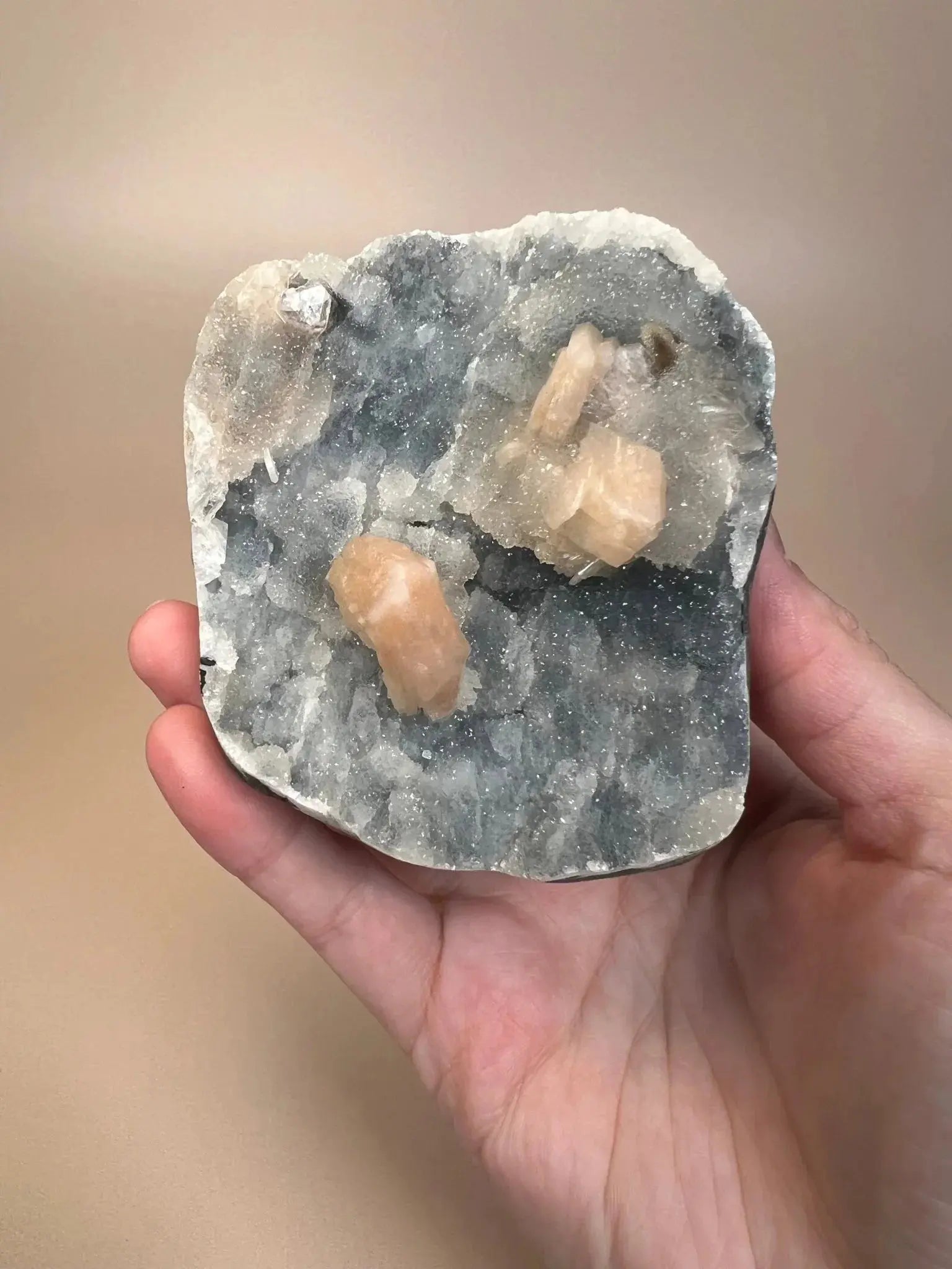 Hand holding icy blue chalcedony with peach stilbite crystals on cut base