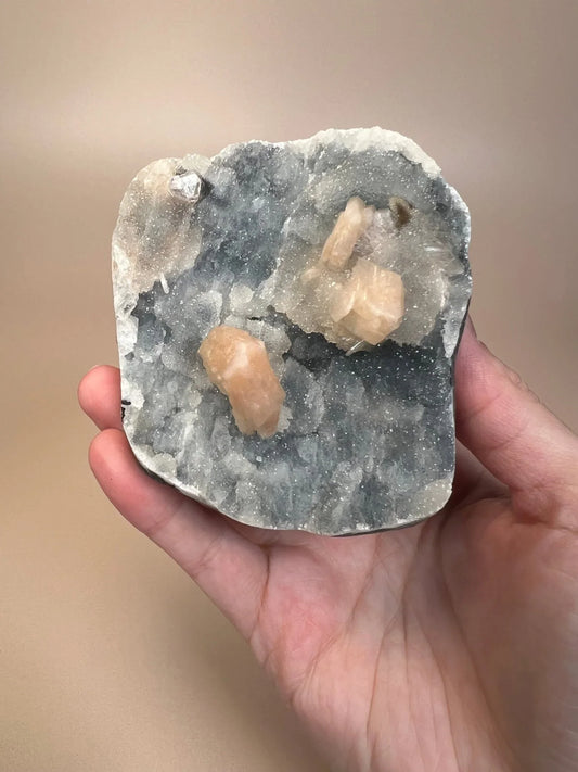 Hand holding icy blue chalcedony with peach stilbite crystals on cut base