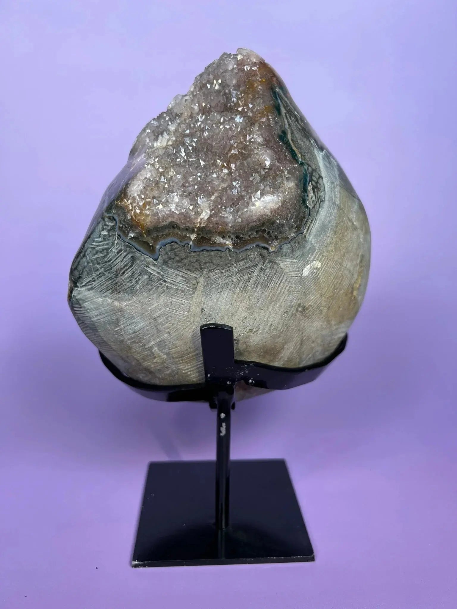 Moody gray rainbow amethyst geode with sparkling crystals on black stand, purple background