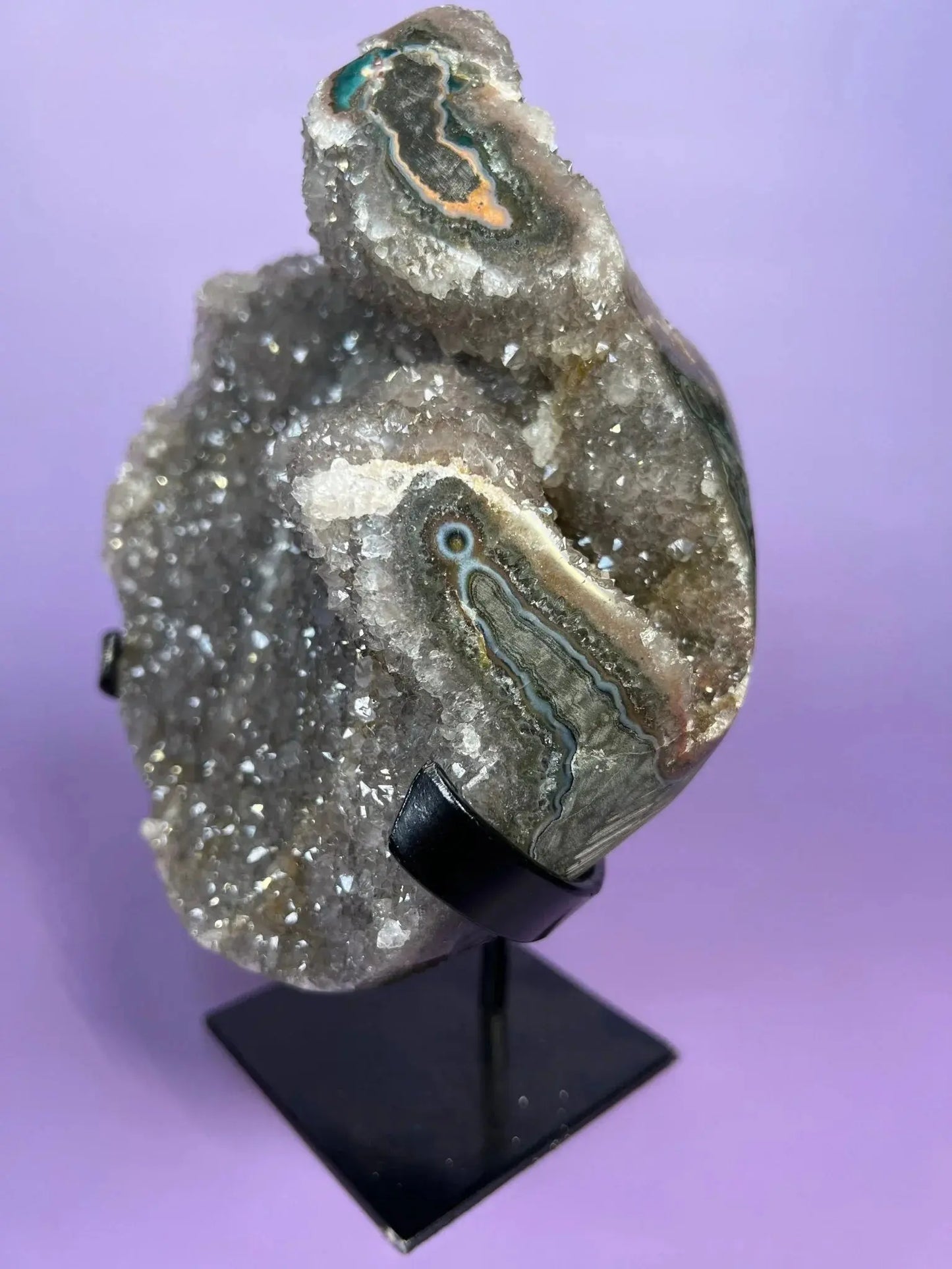 Moody gray rainbow amethyst crystal cluster on black stand with purple background
