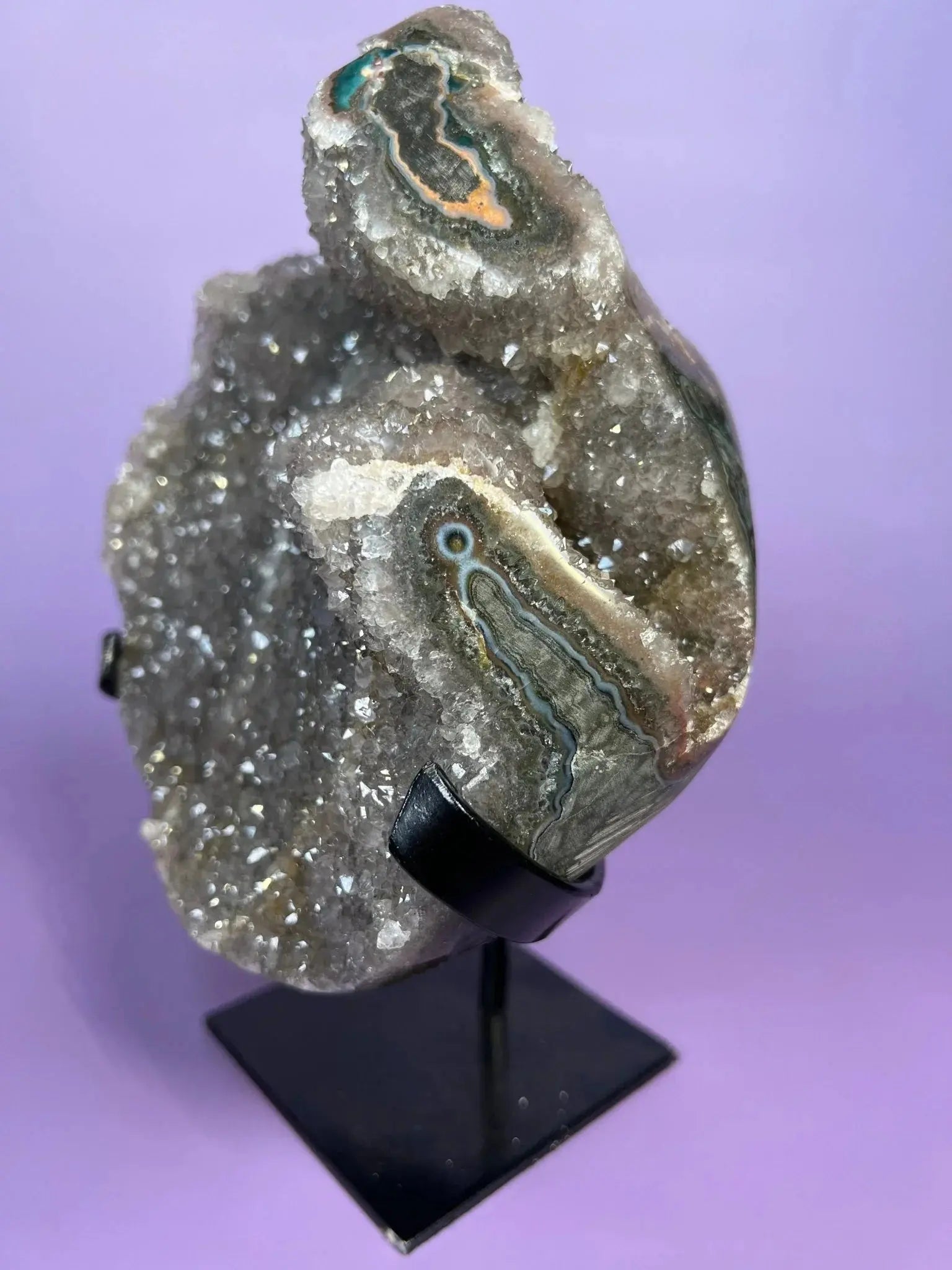 Moody gray rainbow amethyst crystal cluster on black stand with purple background
