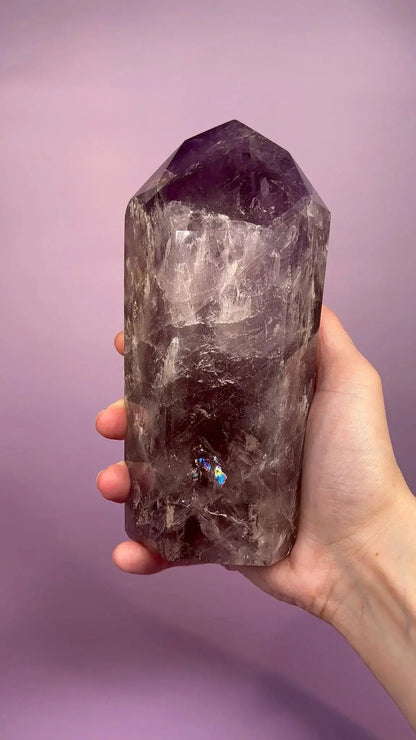 Hand holding a smoky amethyst crystal tower with rainbow flash on a purple background