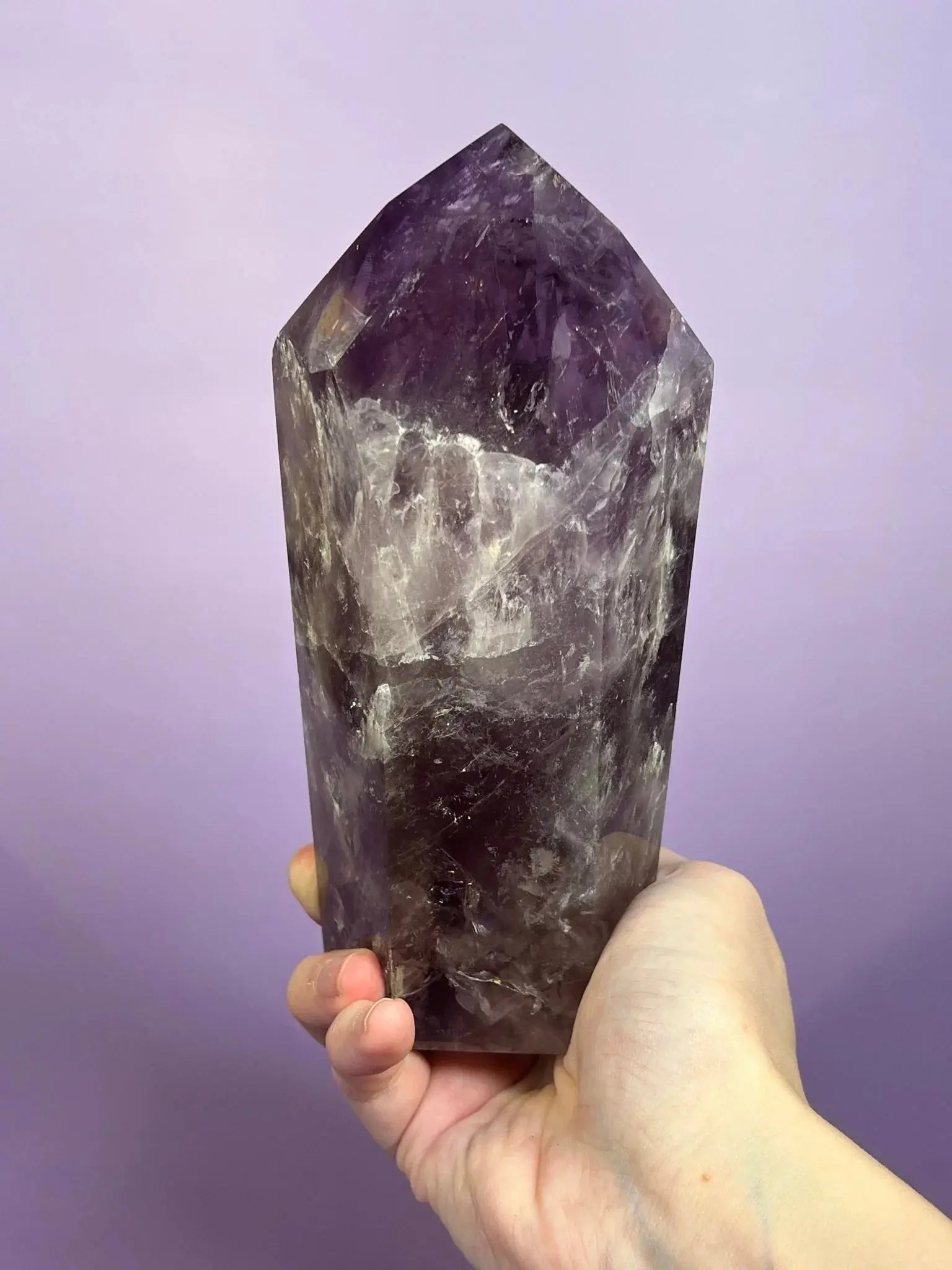 Hand holding a smoky amethyst tower crystal with rainbow flash against a purple background